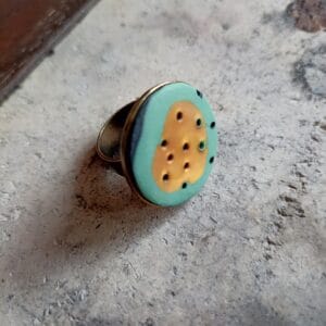 bague plateau, ronde, couleurs vert et or, posée sur un fond en béton.