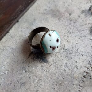 bague ronde , blanche, marron et bleue turquoise posée sur un fond en béton.