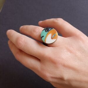 bague ronde, verte, blanche et or, portée sur le doigt d'une main