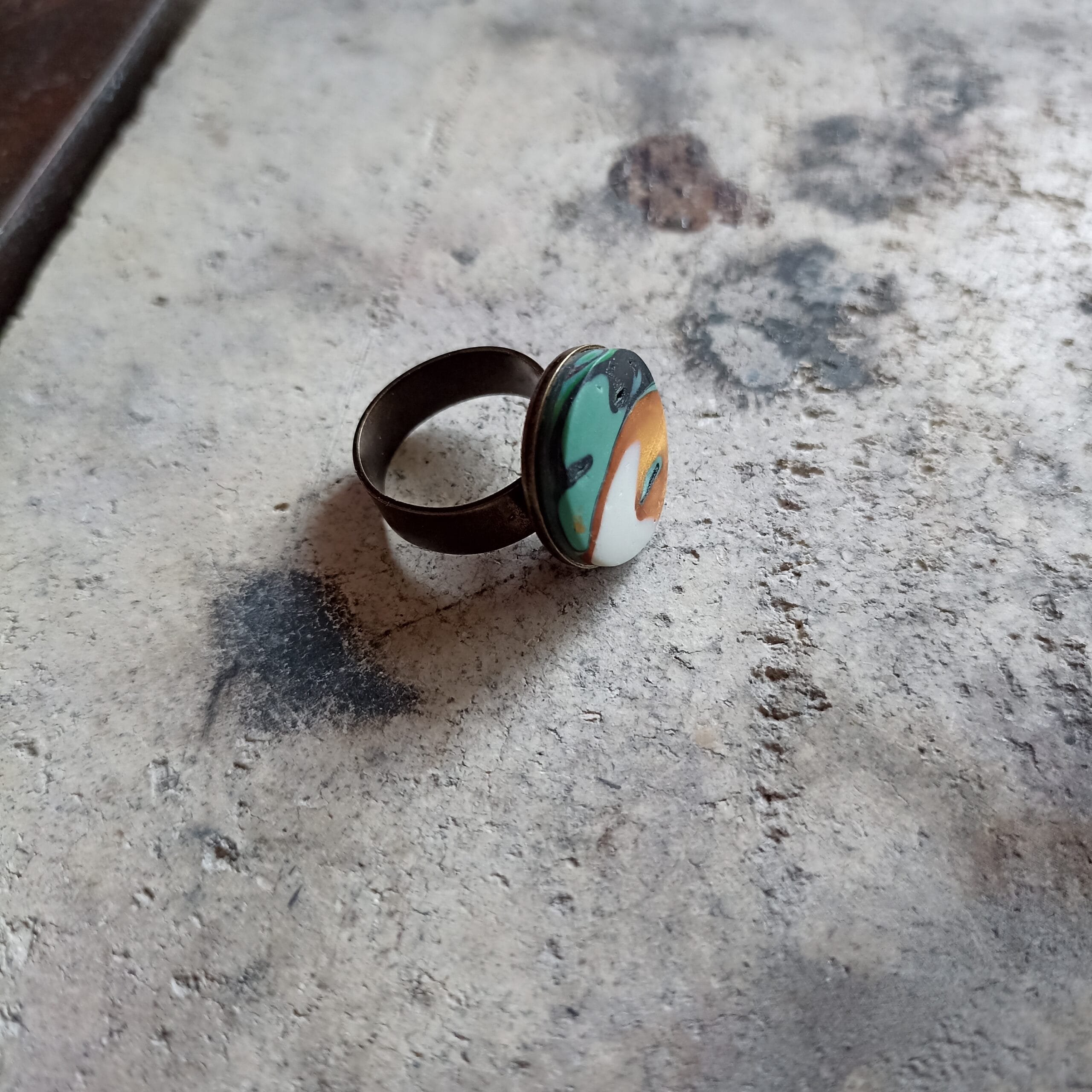 bague ronde verte et or posée sur un fond gris, vue en biais