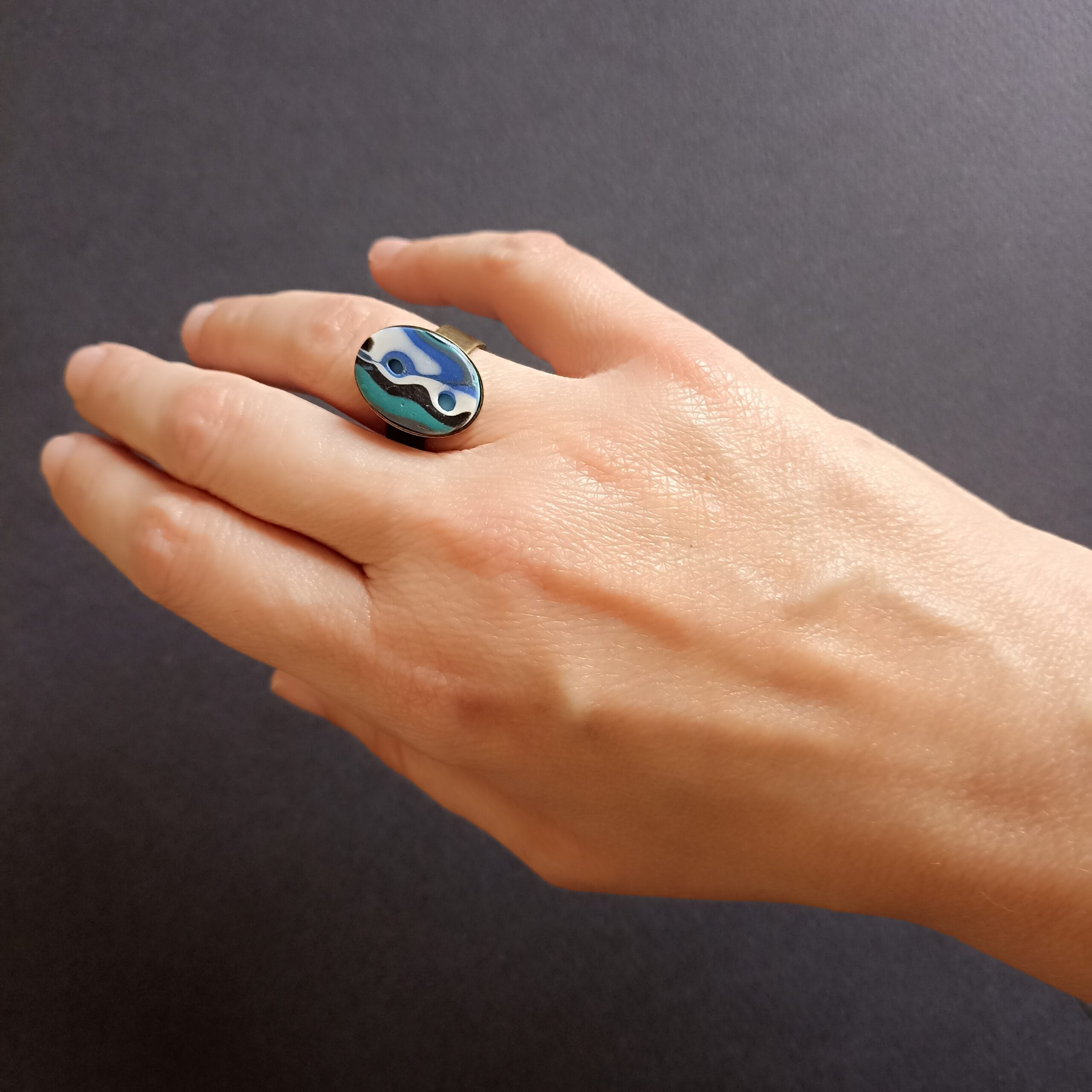 bague ovale bleue et blanche portée sur le doigt d'une main.