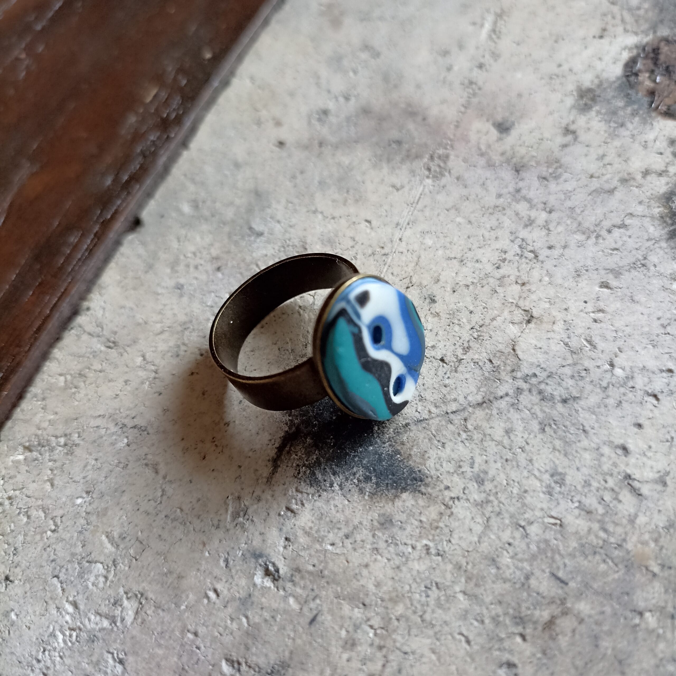 Bague ovale bleue et blanche vue de haut sur un fond gris.