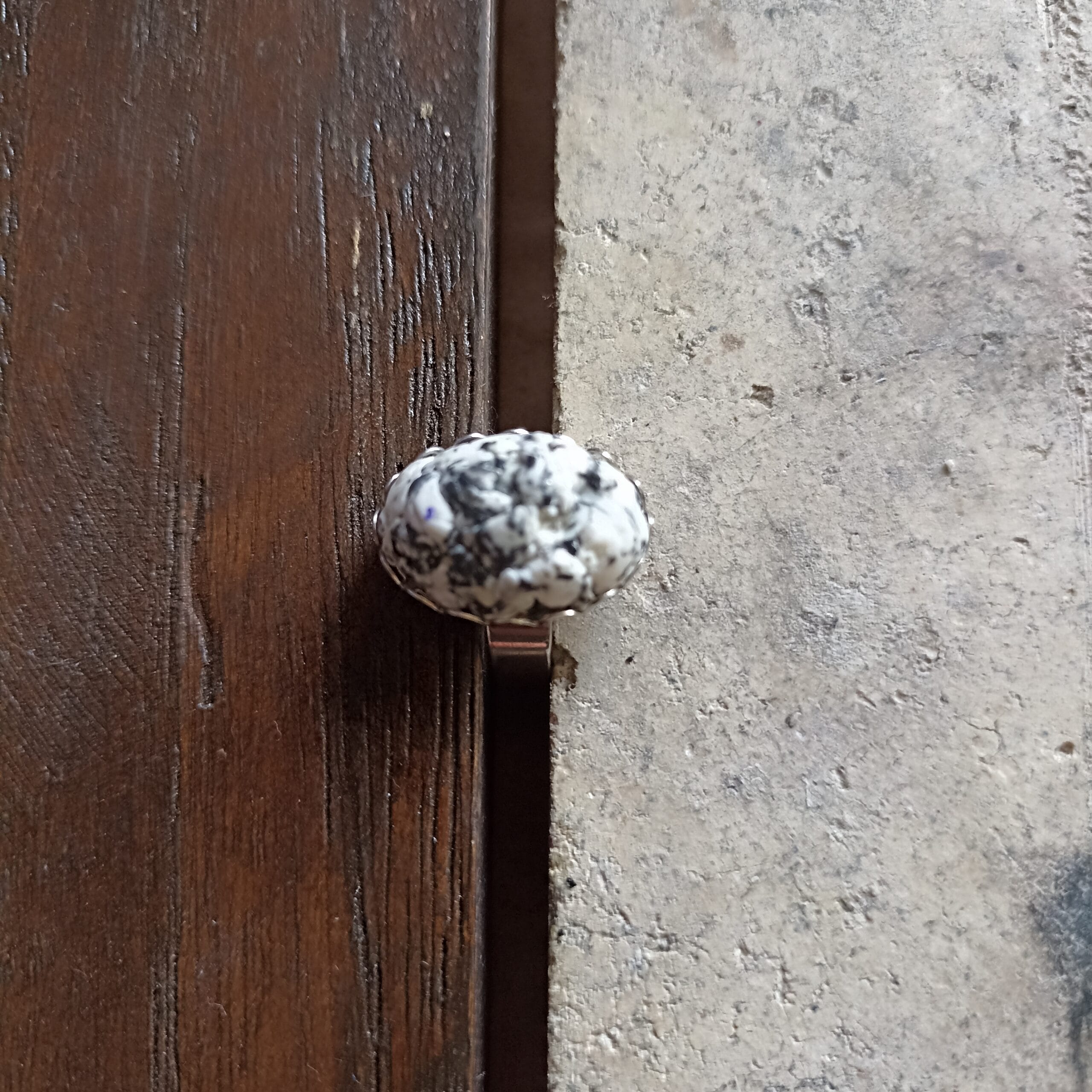 Bague imitation granit vue de dessus, posée sur un fond en bois et en béton.