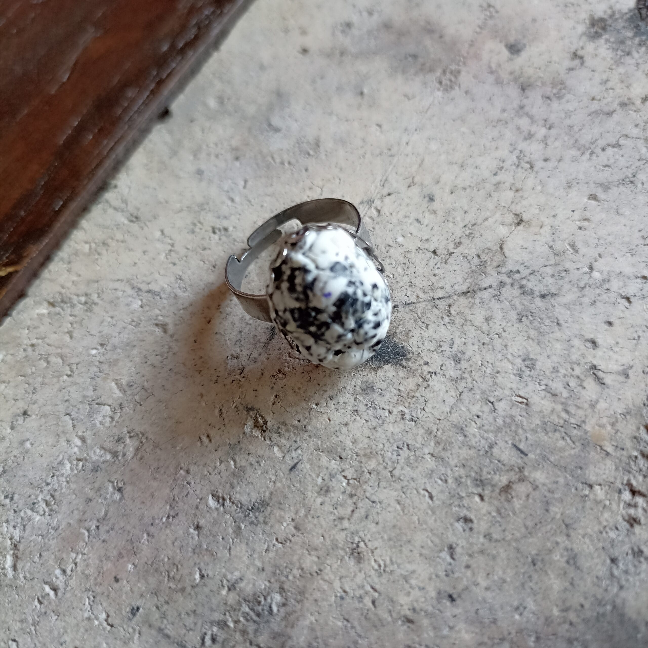 Bague ovale inspirée du granit, posée sur un fond gris en béton.