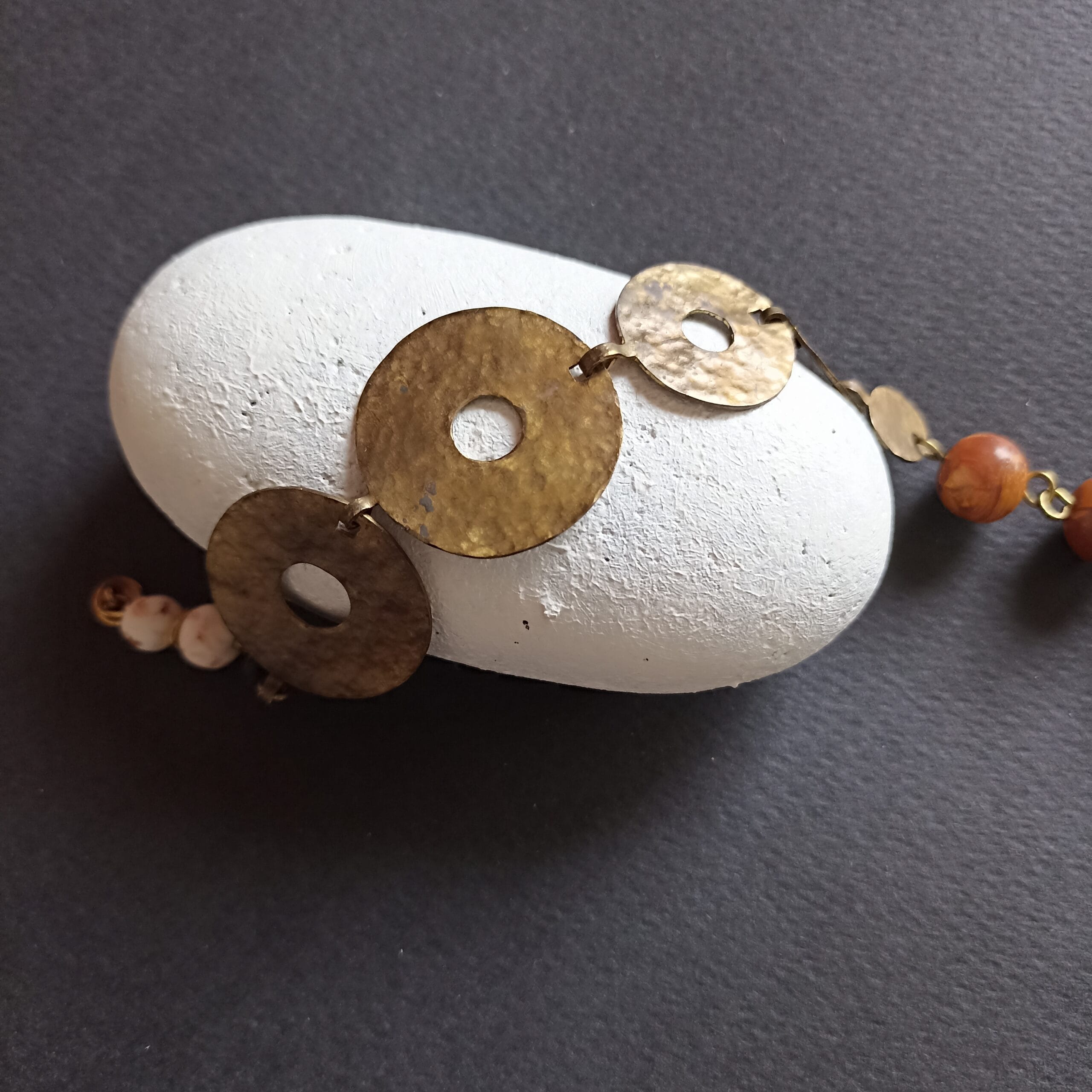 Bracelet Nymphe en laiton posé sur un galet blanc.