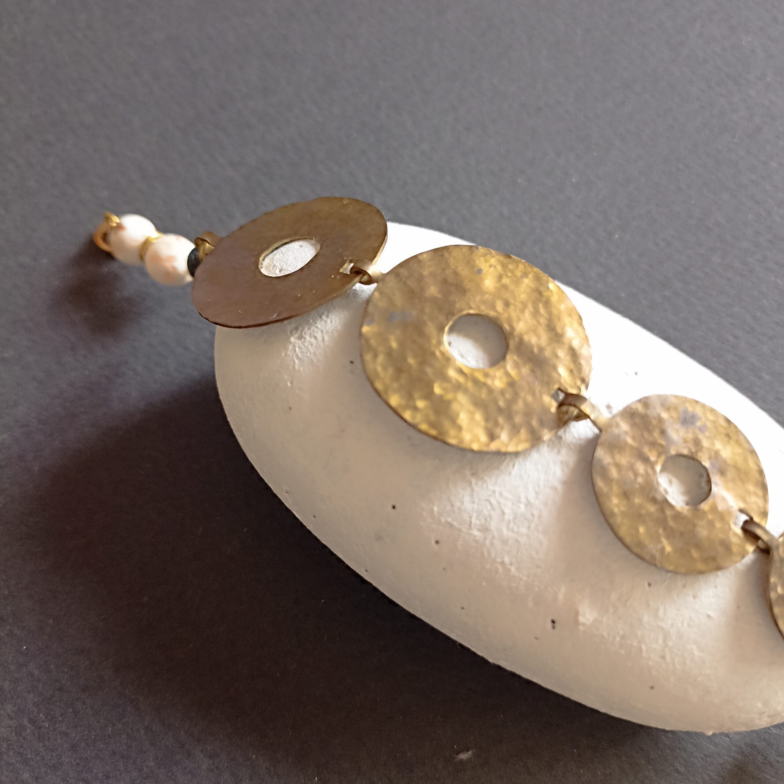 Détail d'un disque en laiton du bracelet Nymphe, posé sur un galet blanc.