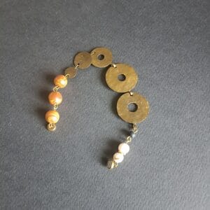 Bracelet Nymphe composé de disques en laiton martelé, posé à plat sur un fond noir.