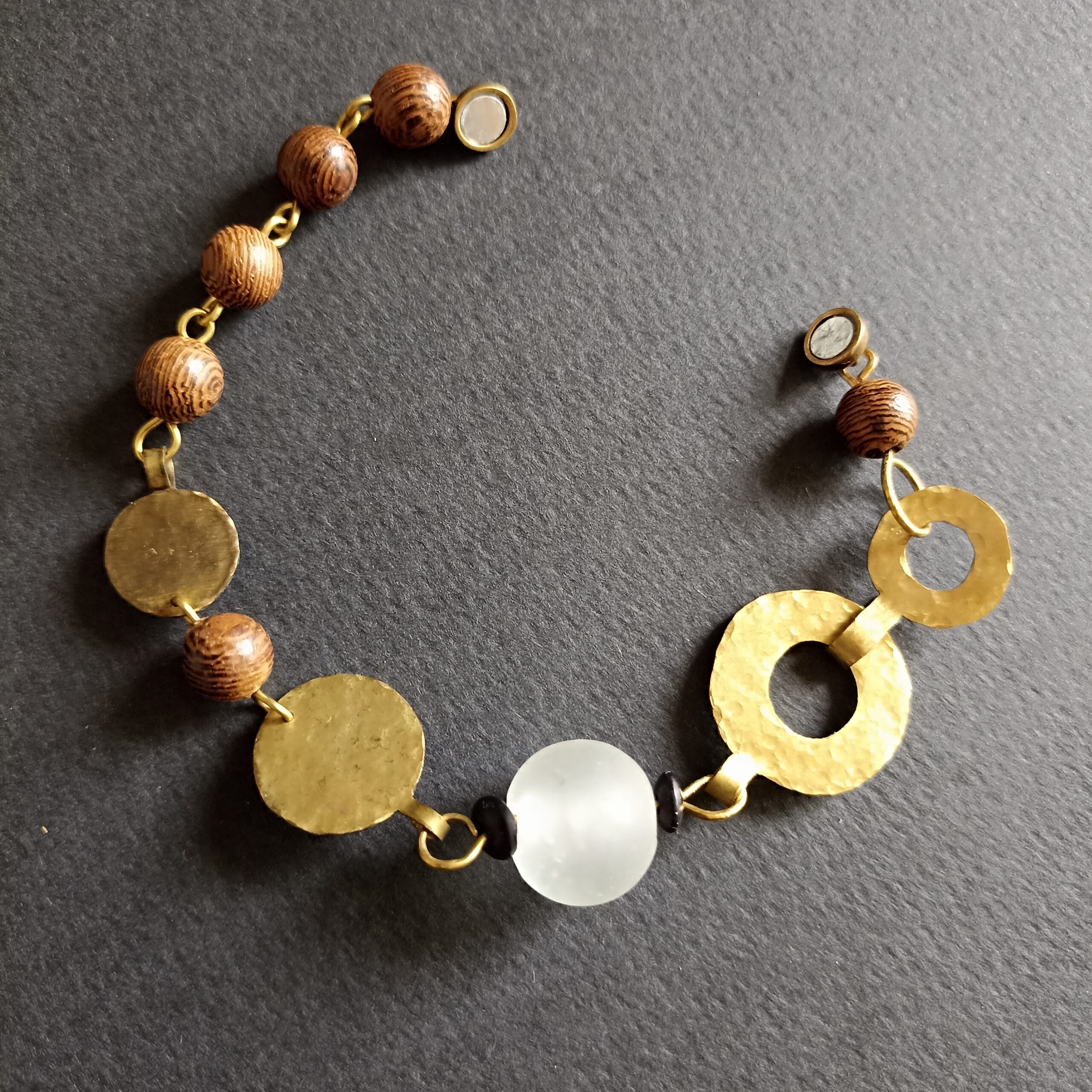 Bracelet Ecume composé de perles en bois, verre et disques en laiton, posé sur un fond noir.