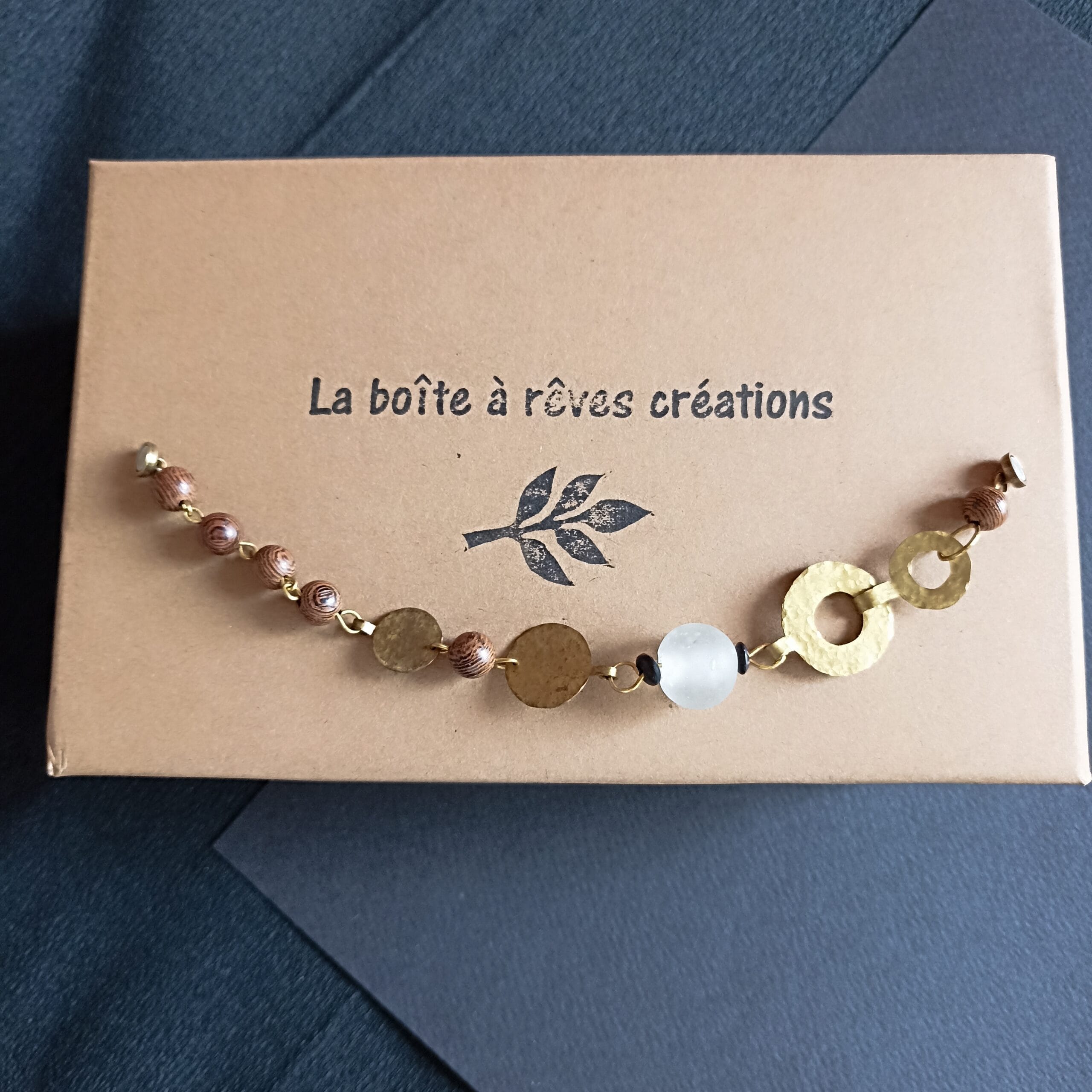 Bracelet Ecume posé sur son écrin en carton au logo de la marque;