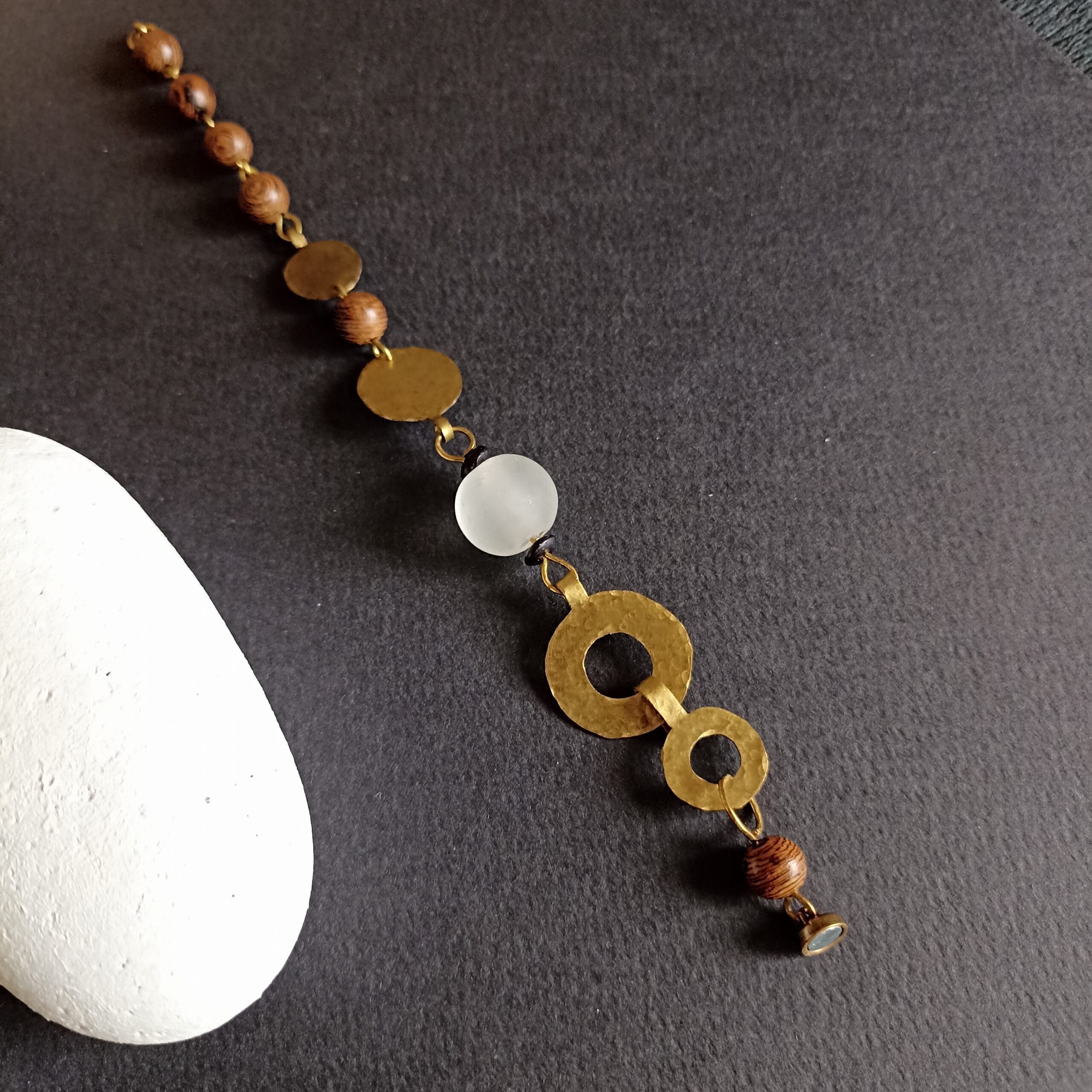 Bracelet Ecume posé sur un fond noir, à coté d'un galet blanc.