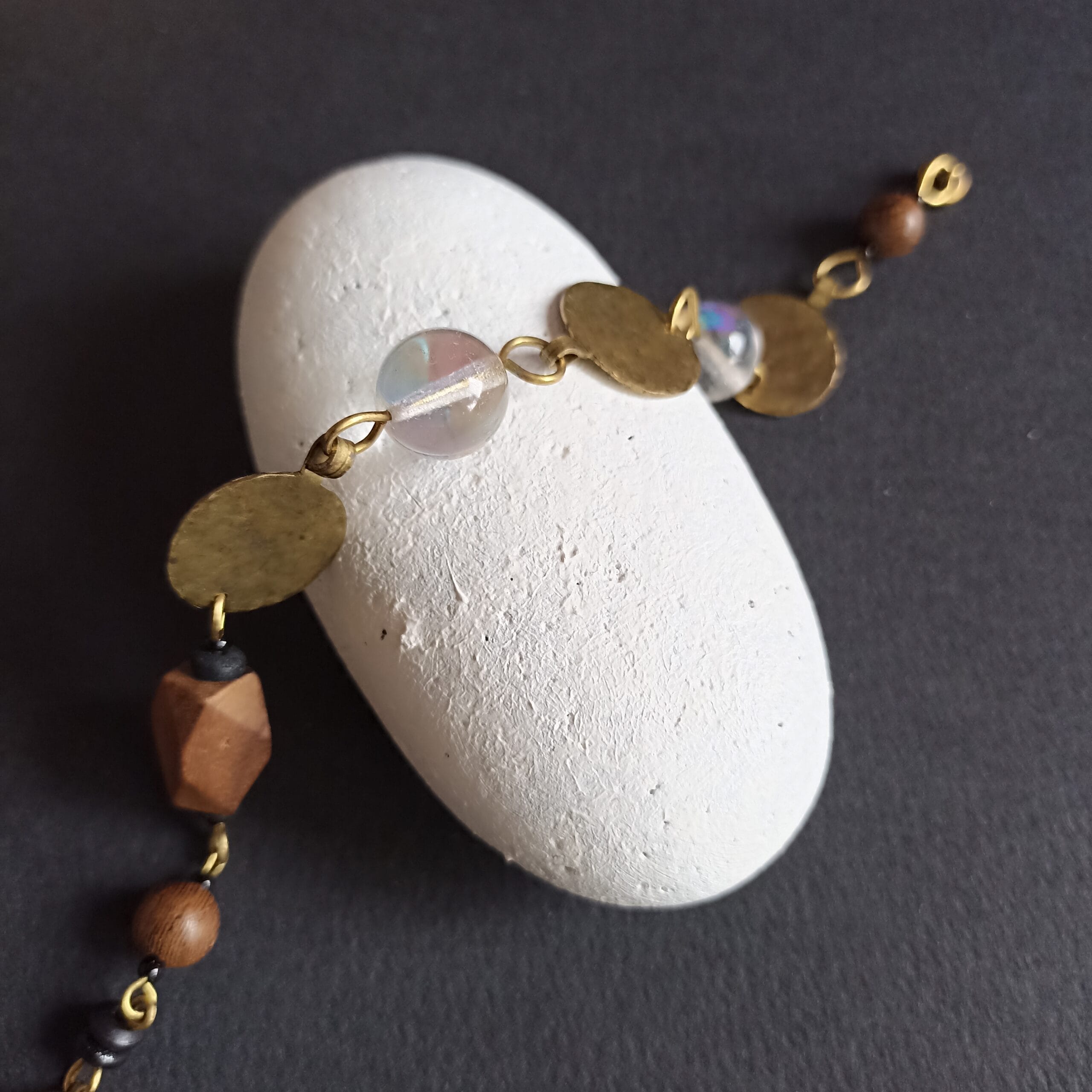 Bracelet Goutte aux perles irisées posé sur un galet blanc sur fond noir.