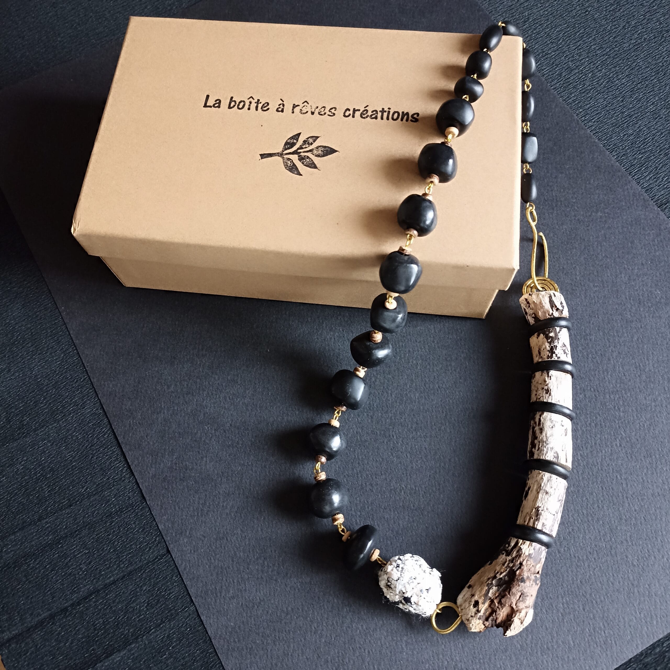 Collier en bois flotté et polymère posé sur son écrin sur fond noir.