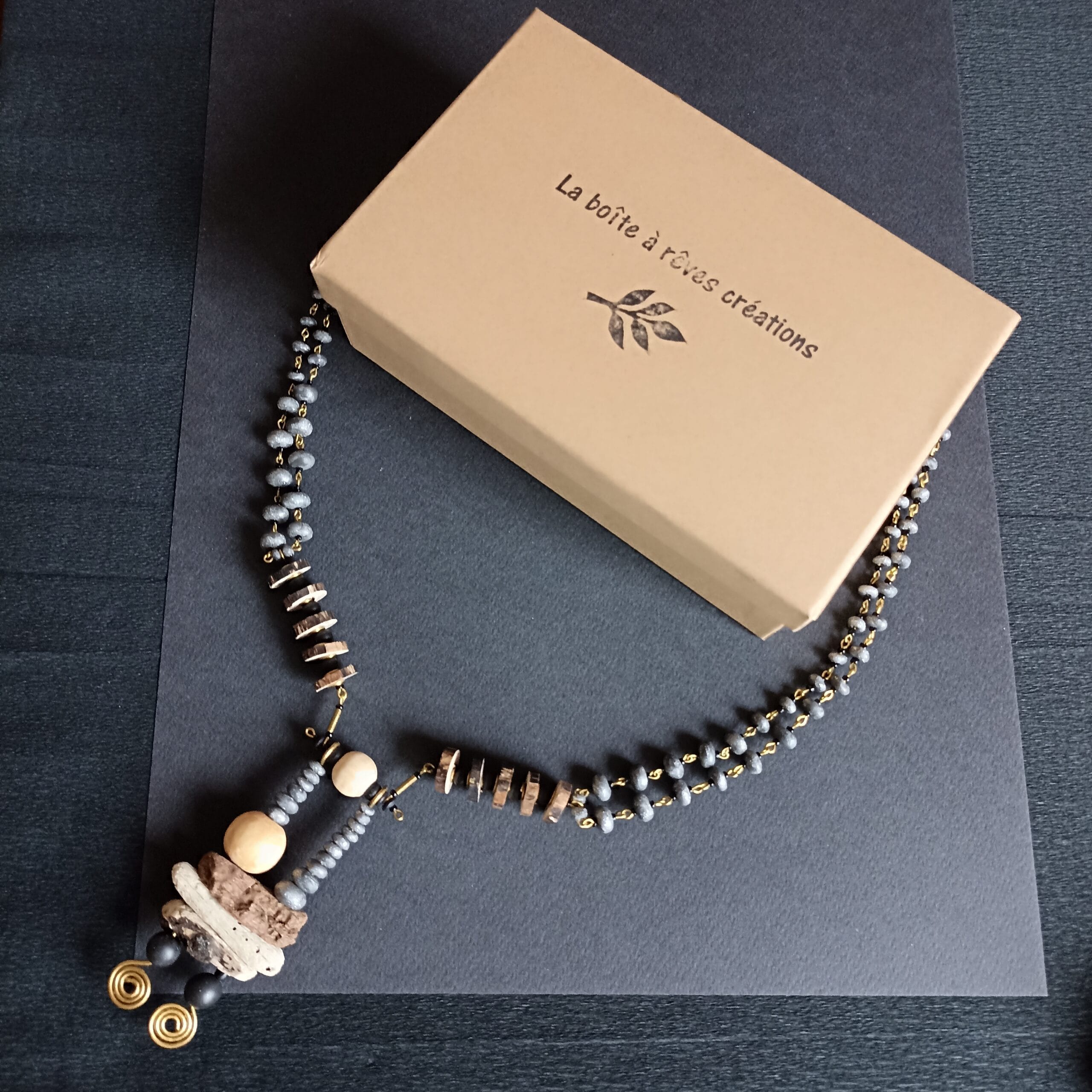 Collier Cairn posé à plat sur fond noir à côté de son écrin.