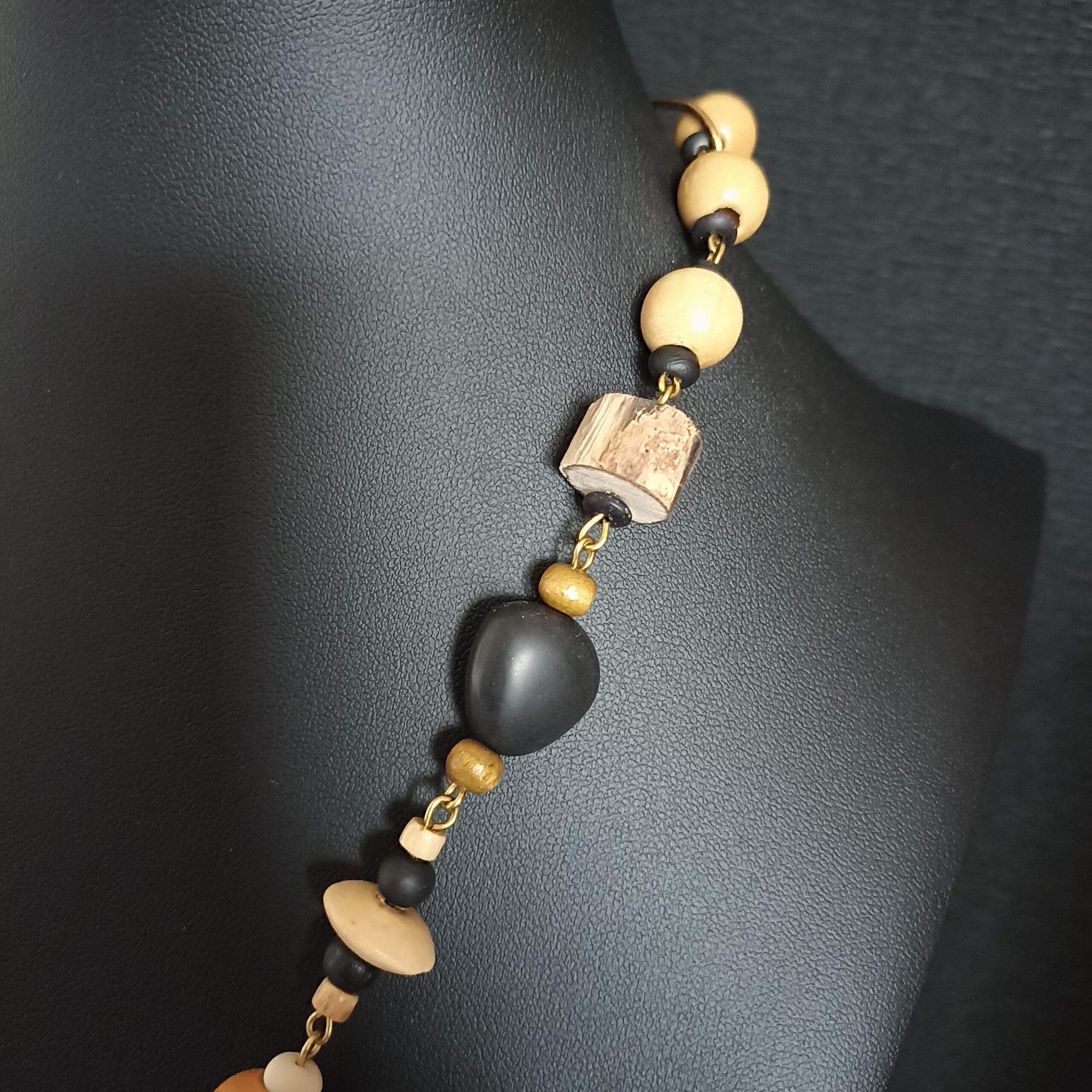 Gros plan sur la chaîne en bois et laiton d'un collier sur son buste de présentation.