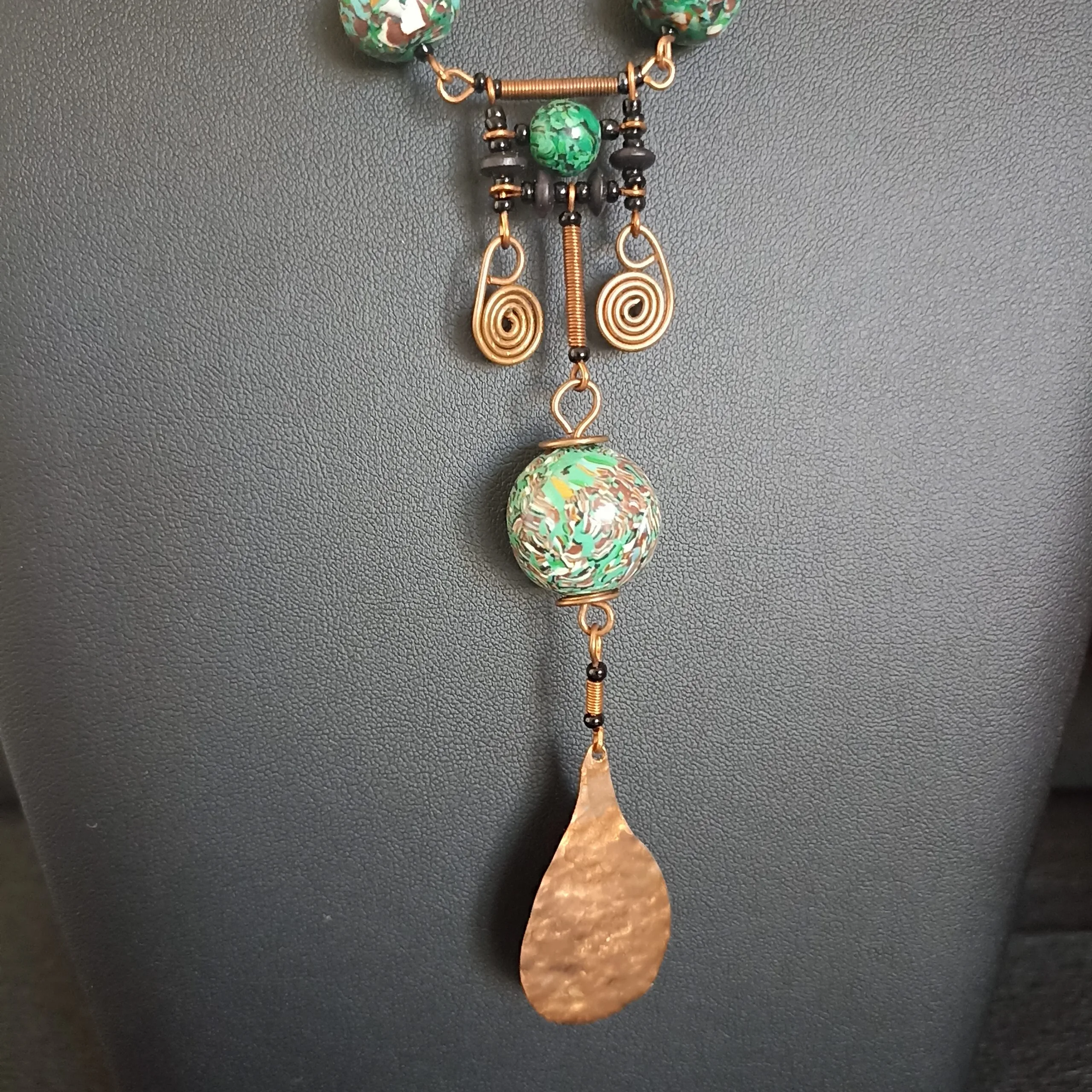 détail du pendentif d'un collier en perles vertes et cuivre martelé.