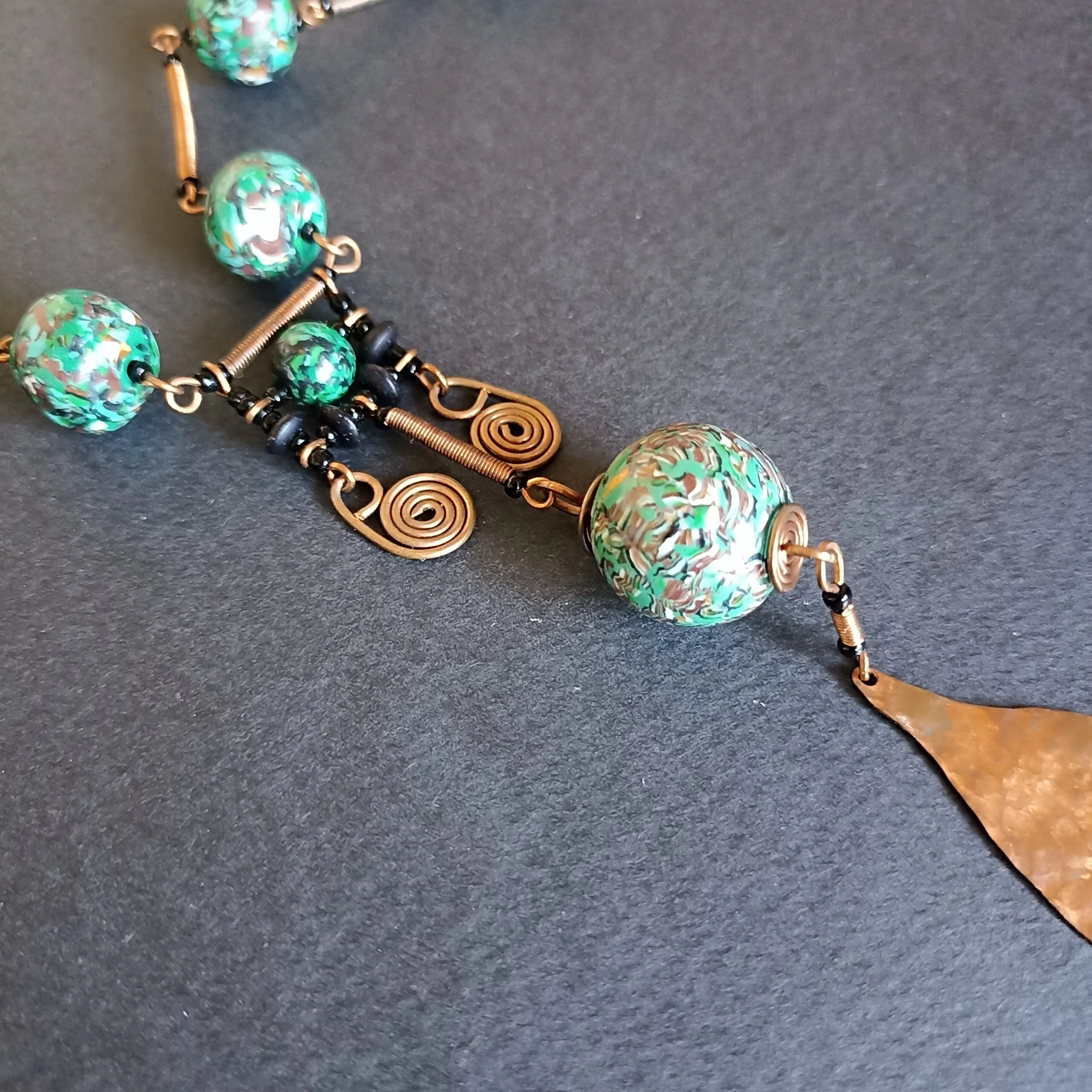 Détail du pendentif d'un collier en perles vertes, posé sur un fond noir.