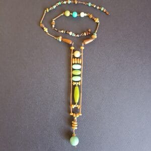 collier dans différents tons de vert, avec un long pendentif vu de haut, posé sur un fond noir.