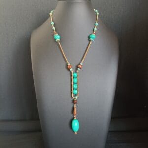 Collier avec pendentif en perles vertes, posé sur un buste de présentation noir.