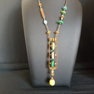 collier long en perles vertes et bois sur un buste de présentation noir, avec un grand pendentif.