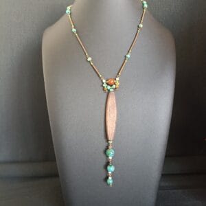 collier rustique avec un long pendentif en bois ovale et des perles bleues, posé sur un buste de présentation.