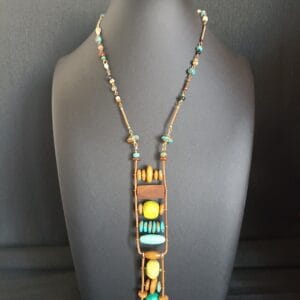 Collier aux couleurs vert et bois avec un long pendentif, posé sur un buste de présentation.